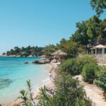 Blick auf das kristallklare Meer und den Strand von einem Ksamil Hotel am Strand, umgeben von üppigem Grün